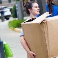 An alumna carrying a big box into a dorm.